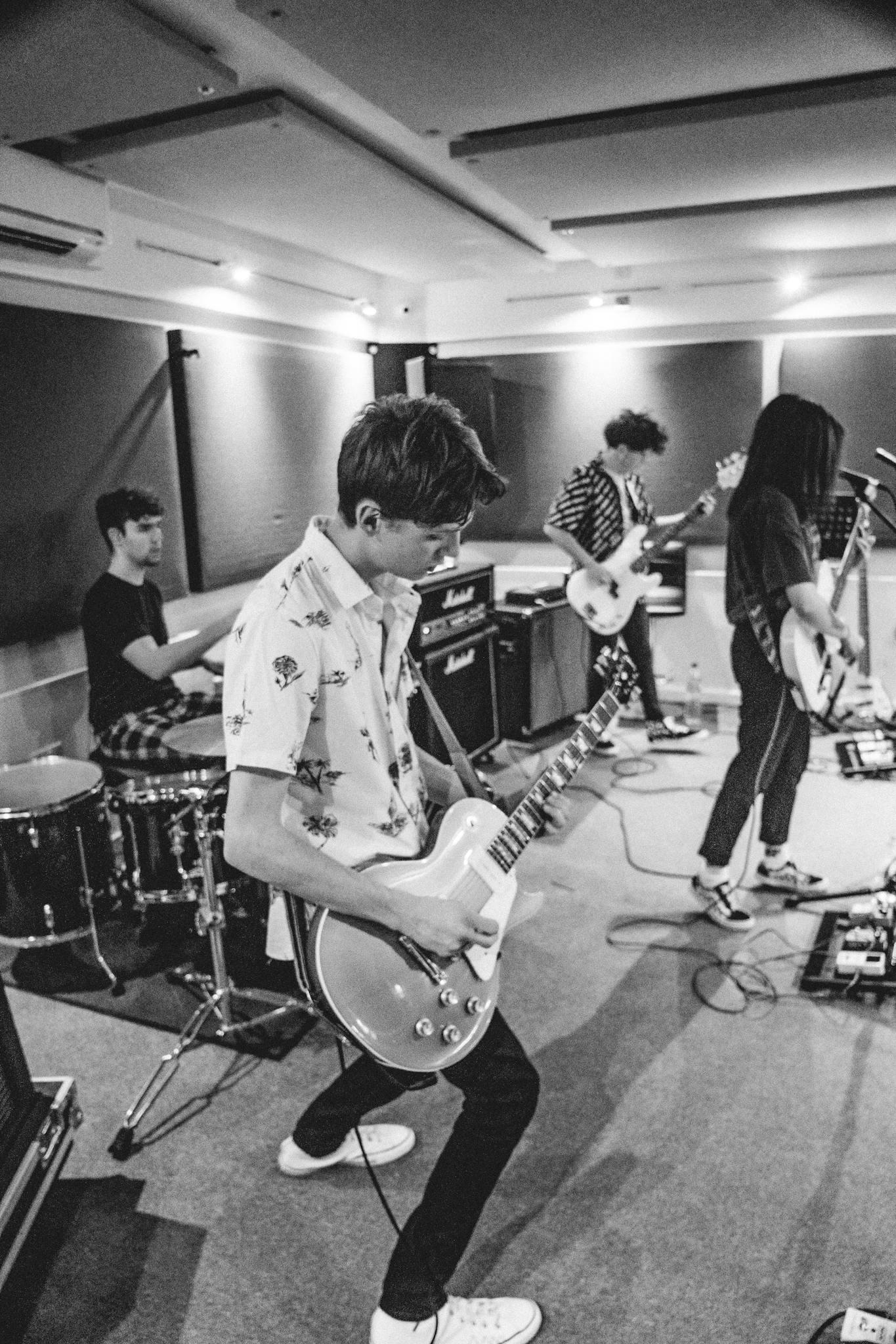 Energetic black and white image of a band rehearsing with electric guitars and drums.